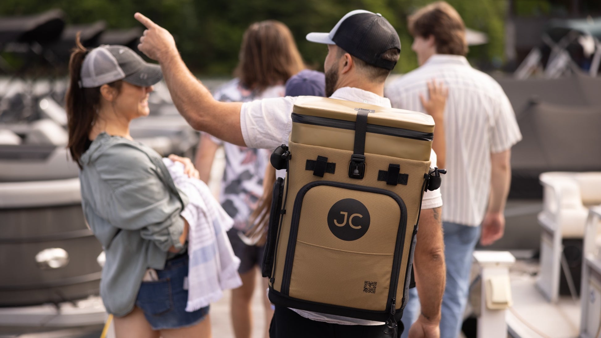 Person carrying a JC branded cooler backpack with people and boats in the background