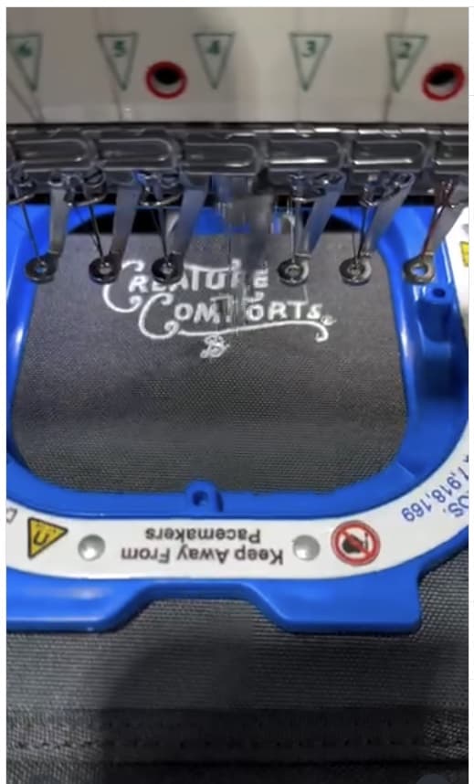 A Creature Comforts logo being embroidered on a JustinCASE bag held in an embroidery frame