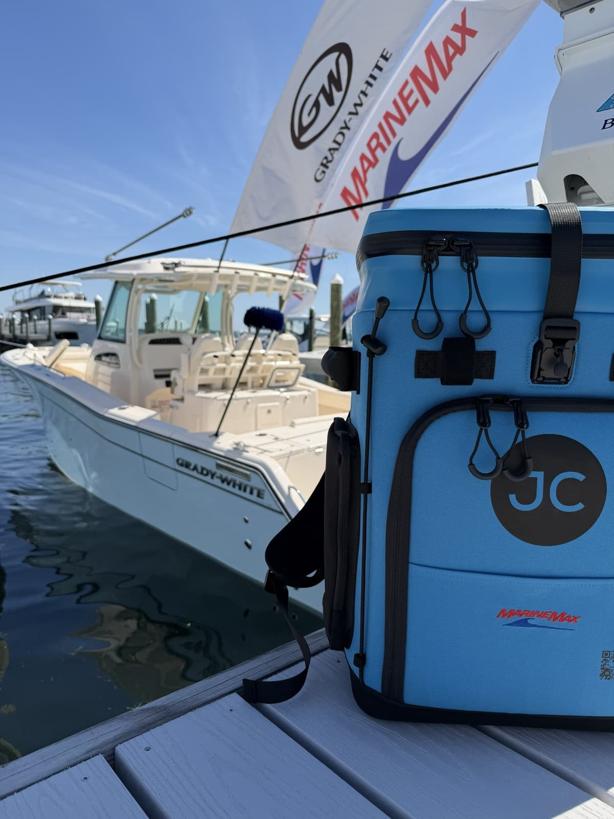 A light blue JustinCASE bag with MarineMax branding on a dock, with a Grady-White boat and MarineMax flags behind it