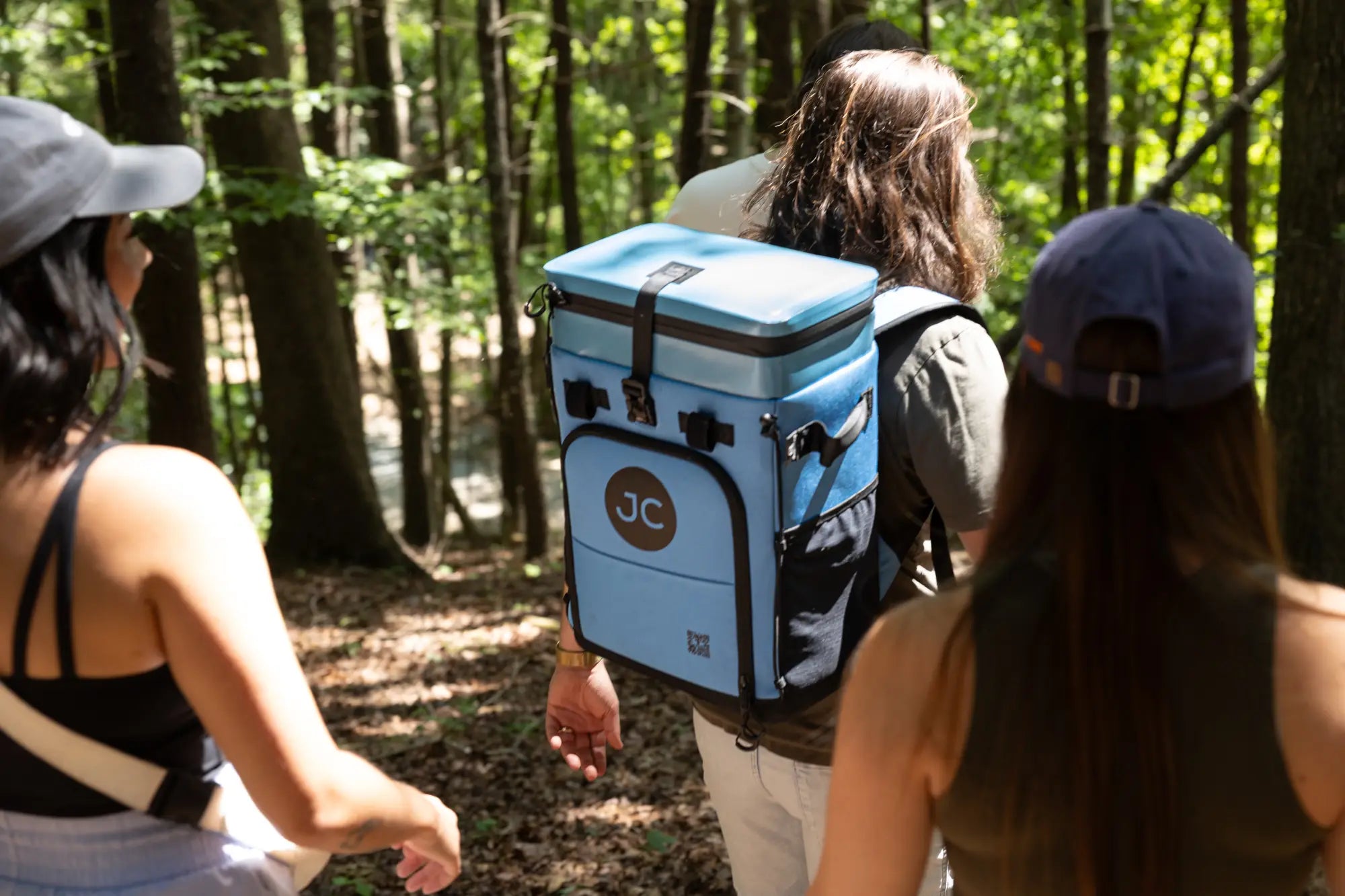 Person carrying a blue JC cooler bag through a forest